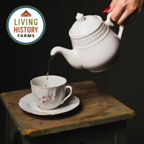 Tea pours from a white pot into a waiting cup. A logo for Living History Farms is in the top left corner.