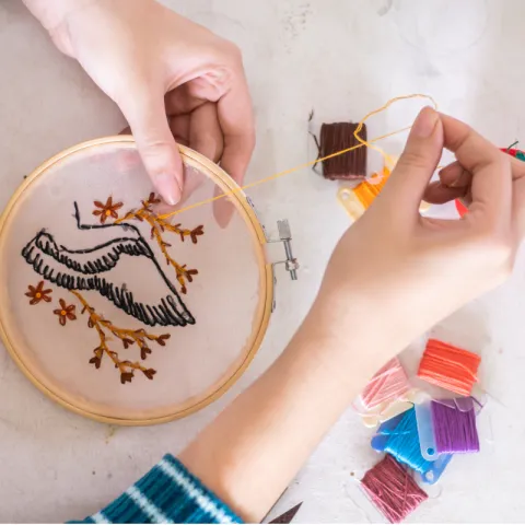 Two hands use a needle to create an embroidered landscape.
