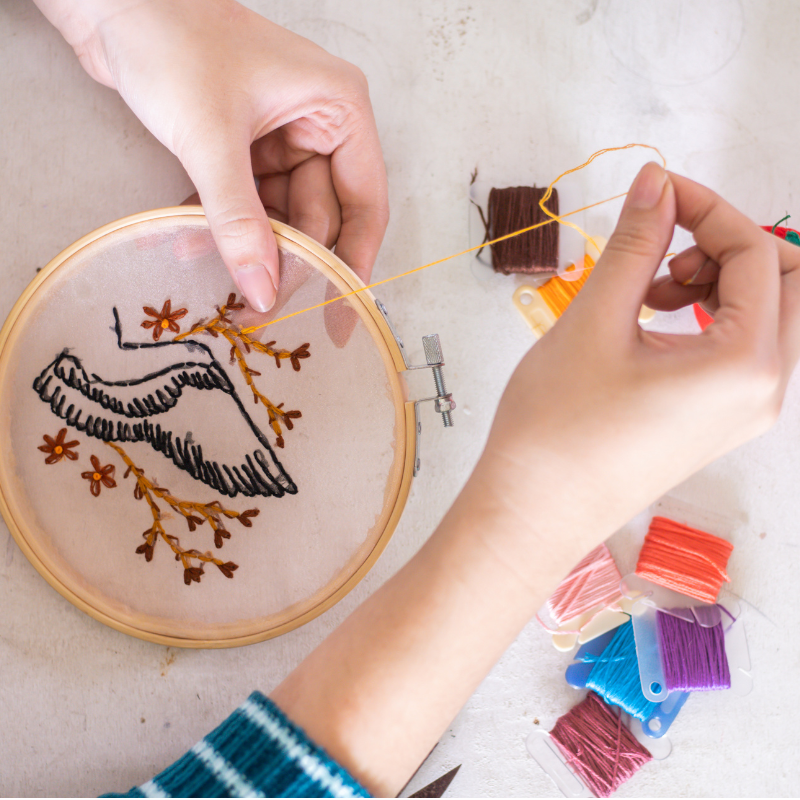 Two hands use a needle to create an embroidered landscape.