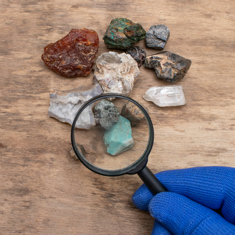 gloved hand holding magnifying glass to rocks